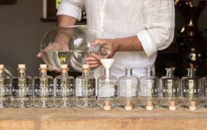 Aejist Gin, Mann im weißen hemd befüllt 10 Flaschen über einen weißen Trichter mit Gin