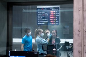 several persons in a climatic chamber with mask behind a glass wall